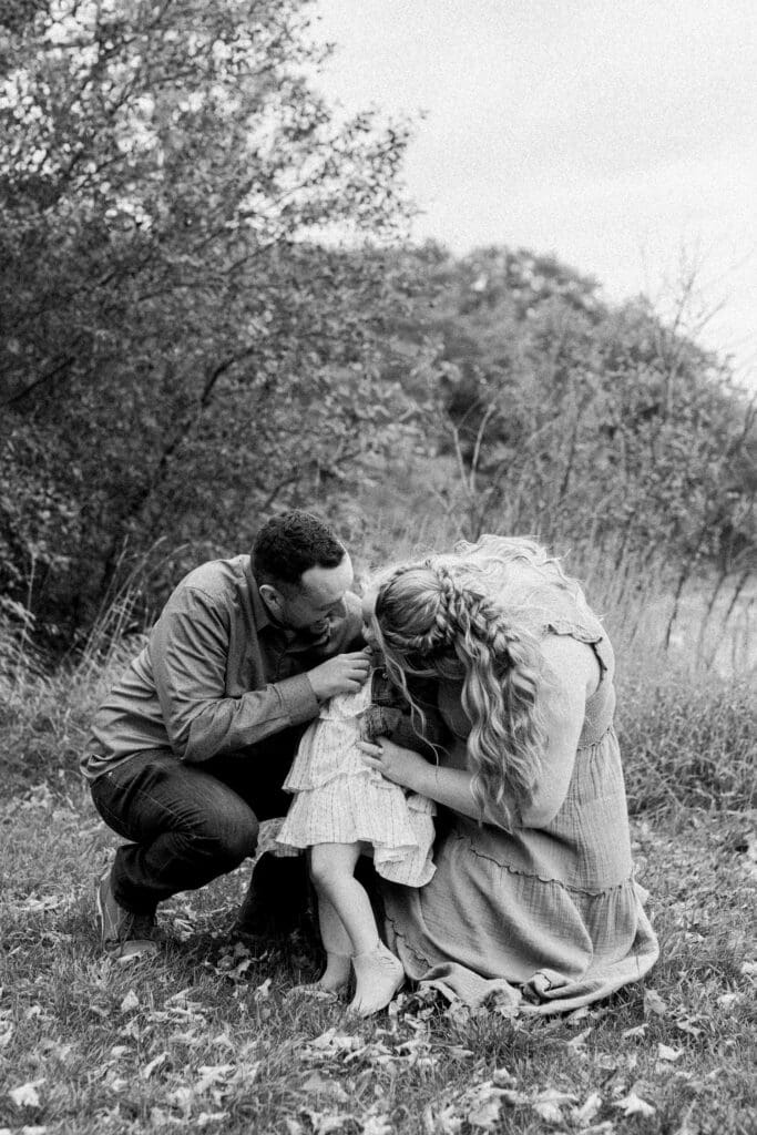 Black and white image of parents sitting on the ground, embracing their daughter tightly.