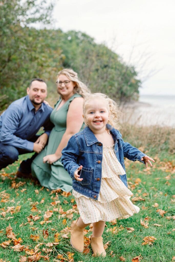 Family of three crouched together on the ground surrounded by autumn leaves.
