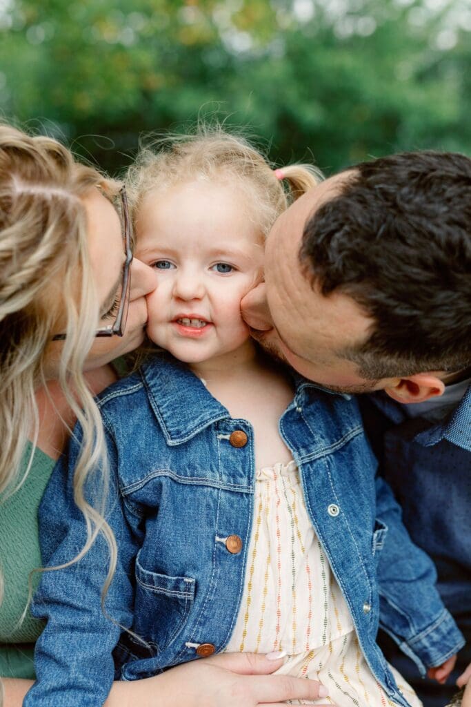 Parents kissing their daughter’s cheeks as she beams with joy.