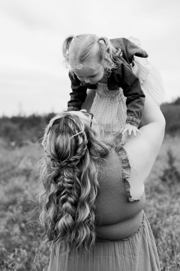 Mother lifting her daughter into the air in a field.