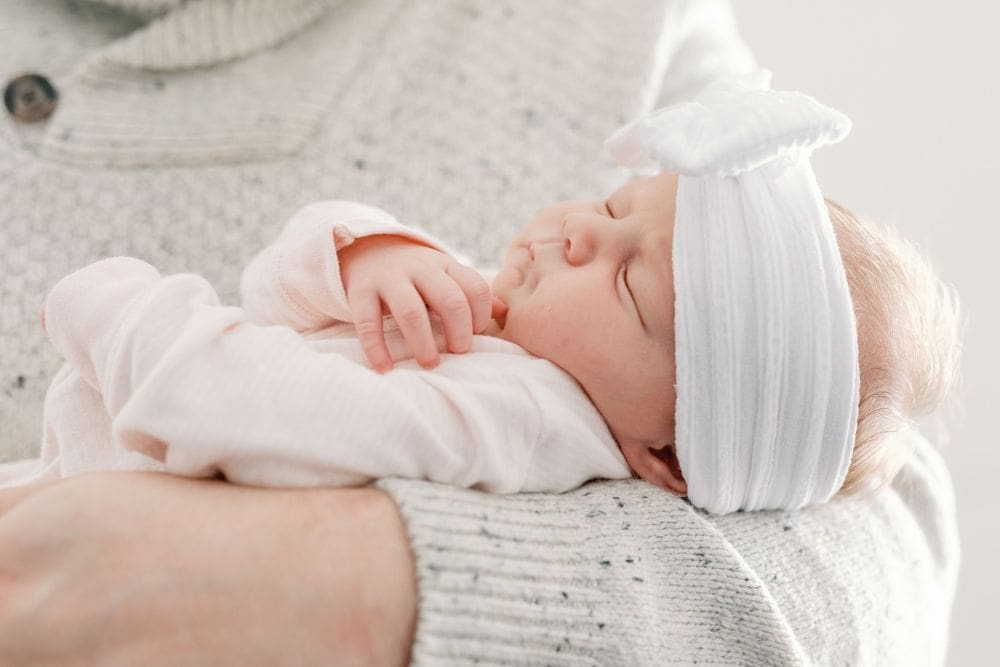 Newborn baby girl sleeping peacefully in a pink sleeper and white bow headband