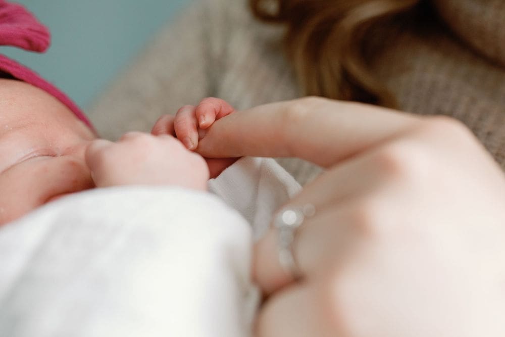 Close-up of a newborn hand gently grasping a parent's finger with an engagement ring visible.