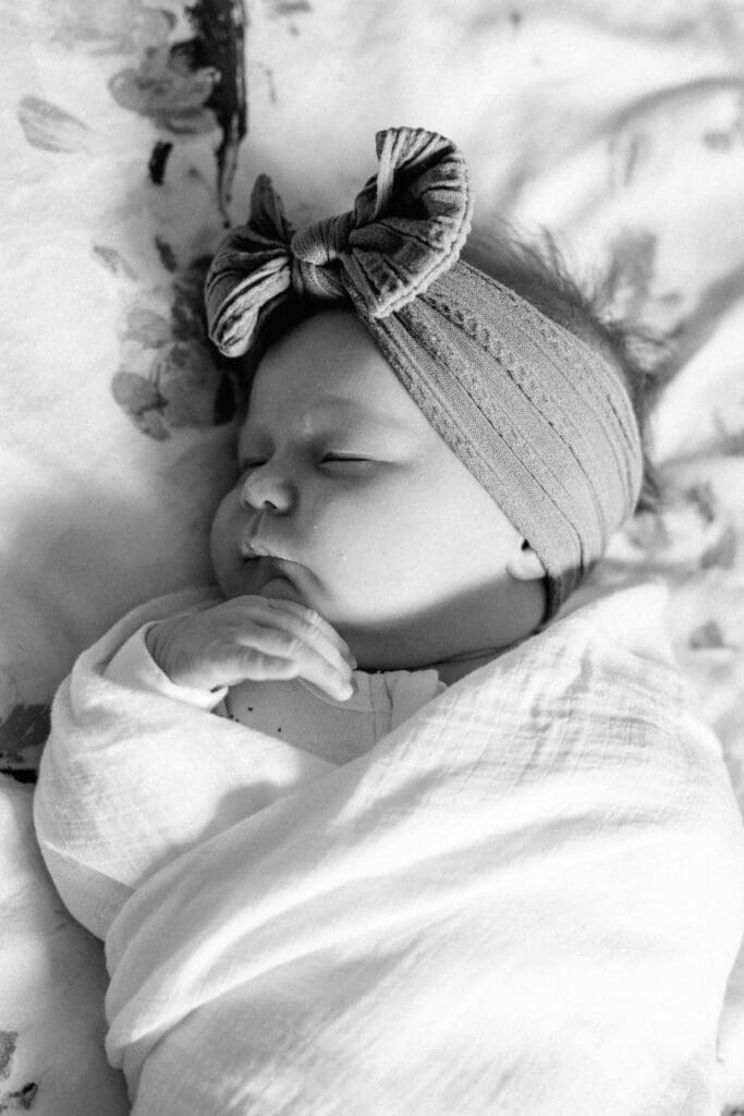 Black and white image of baby girl sleeping in a bow on a floral sheet