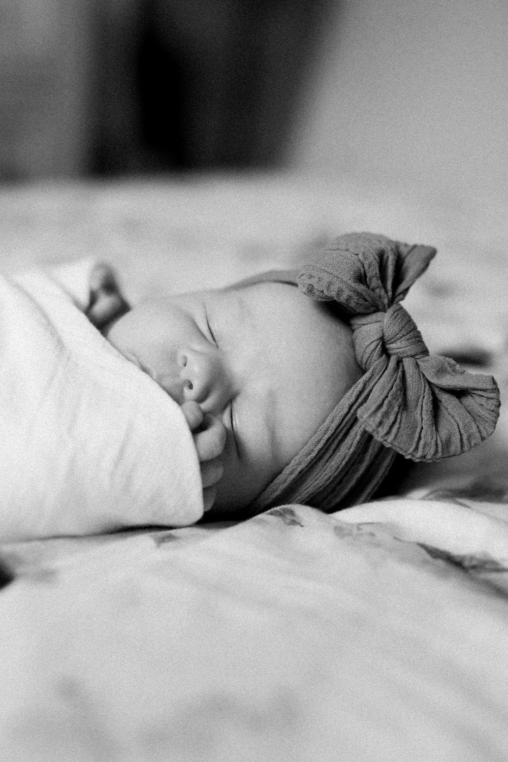 Black-and-white photo of a sleeping newborn wrapped in a soft swaddle with a bow headband.