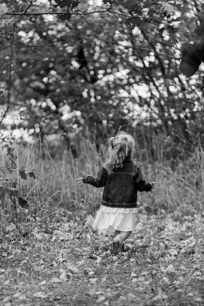 Little girl running through tall grass with wind in her curls.