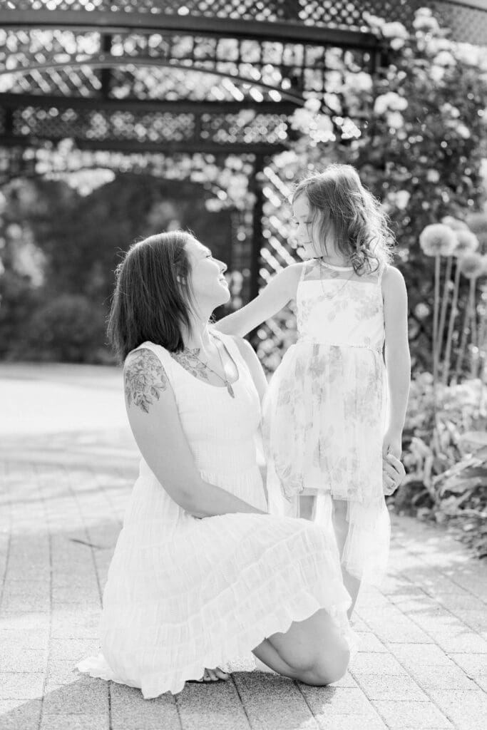 Mother kneeling and smiling at daughter during a garden session in black and white.