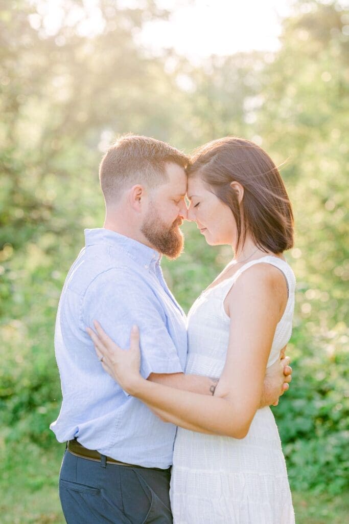 Couple holding each other with foreheads touching during golden hour in the garden.