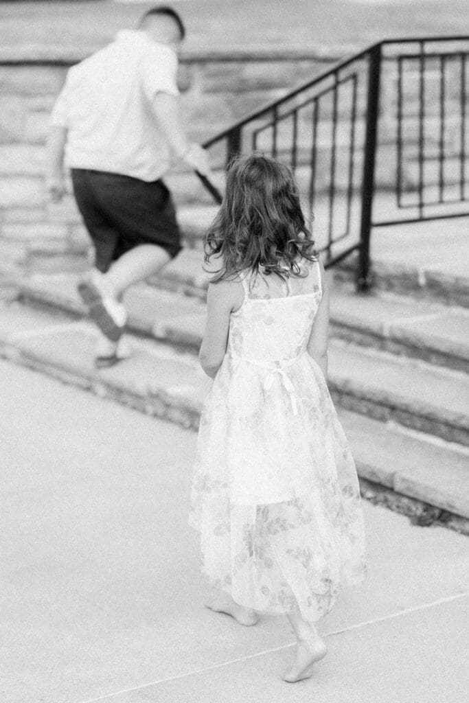 Black and white image of girl following her brother up stone steps during a family session.