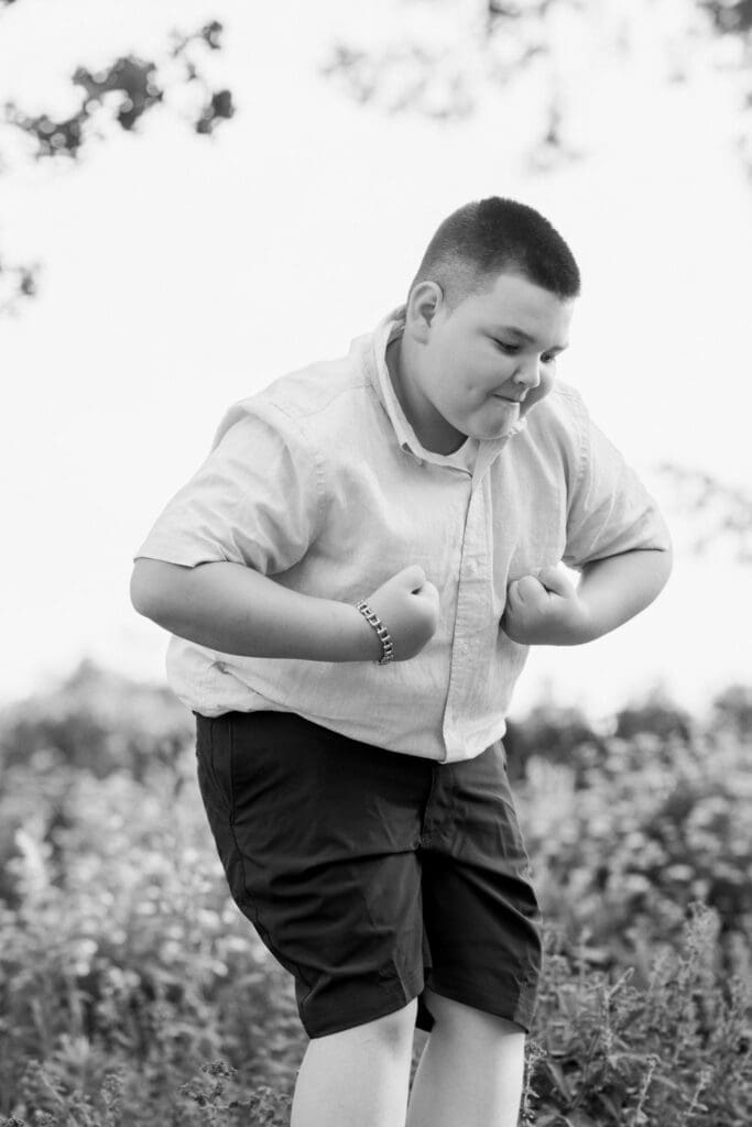 Black and white portrait of a boy striking a playful pose in a garden.