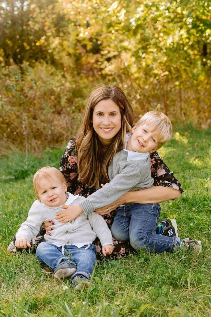 Mom smiling as she embraces her two young sons on the grass