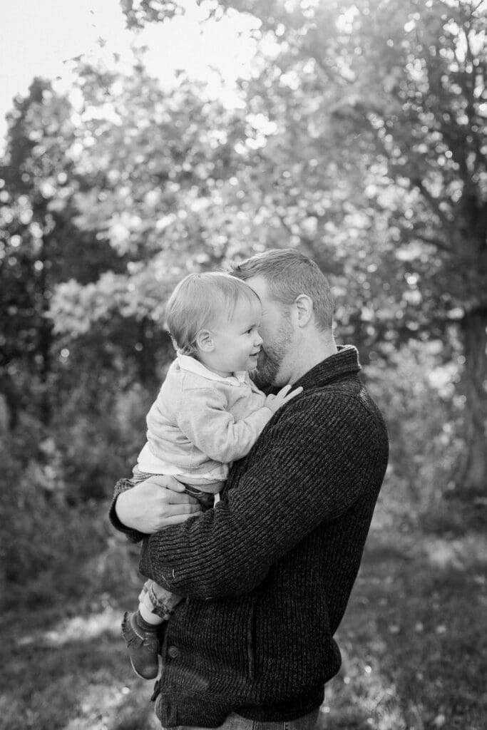Black and white photo of a father gently holding and nuzzling his toddler son outdoors