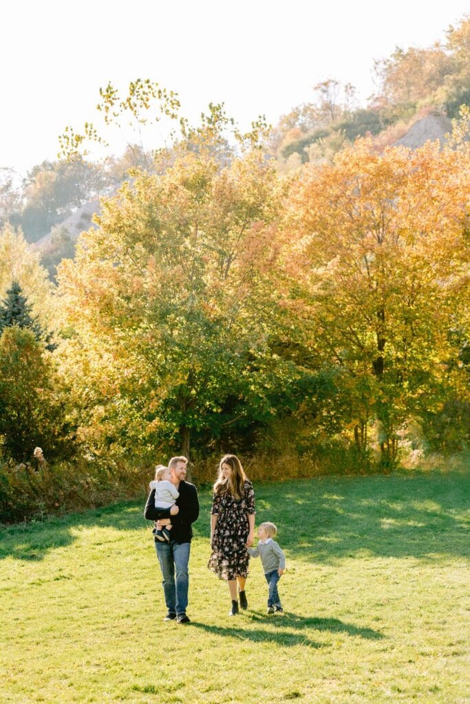 Family walking through an open green field surrounded by vibrant autumn trees