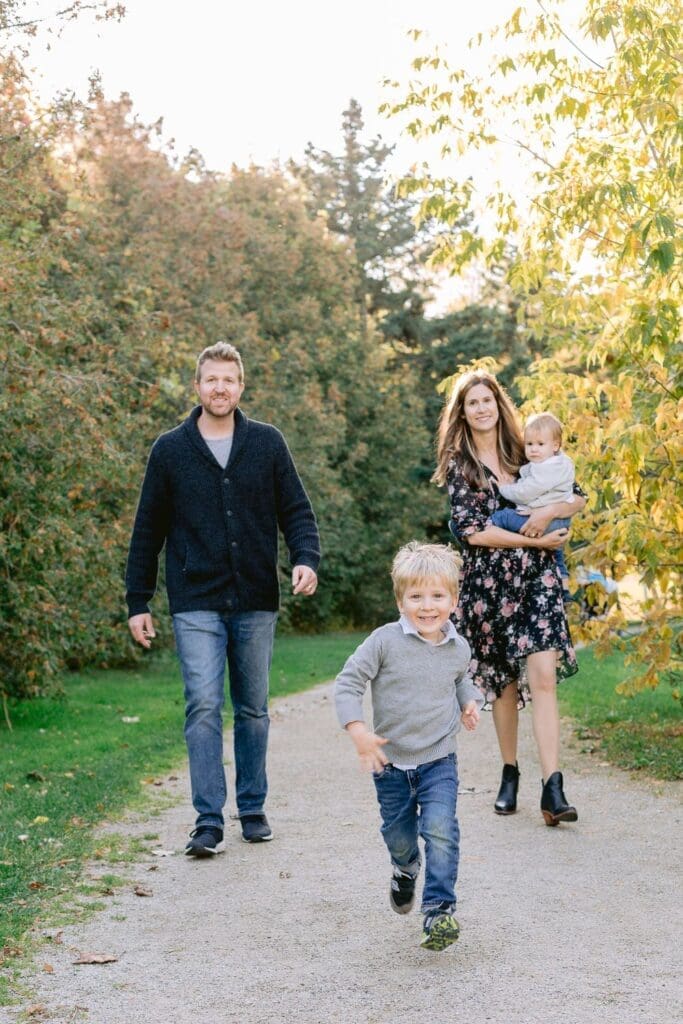 Young boy running ahead of his smiling parents and baby sibling during a family walk on a forested path