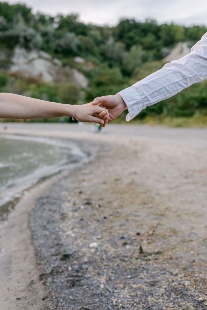 Close-up of couple holding hands near shoreline at Scarborough Bluffs