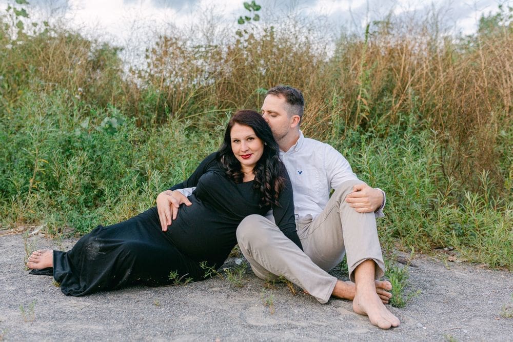 Couple sitting barefoot in wild grass during sunset at Scarborough Bluffs maternity session