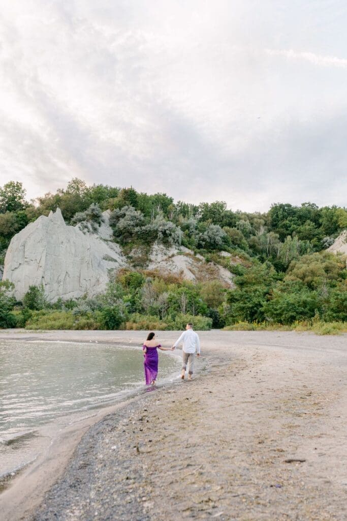 Pregnant woman in vibrant purple gown standing on sandy shore with Scarborough Bluffs in background