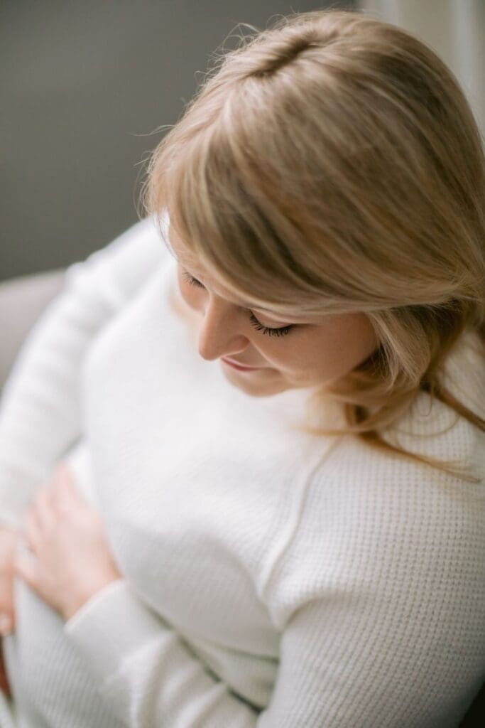 Soft-focus image of a pregnant woman looking down at her belly while sitting in a bright room.