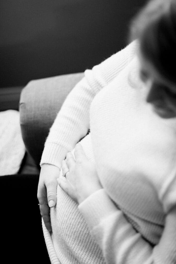Black and white photo of a pregnant woman’s belly with hands resting gently over it.
