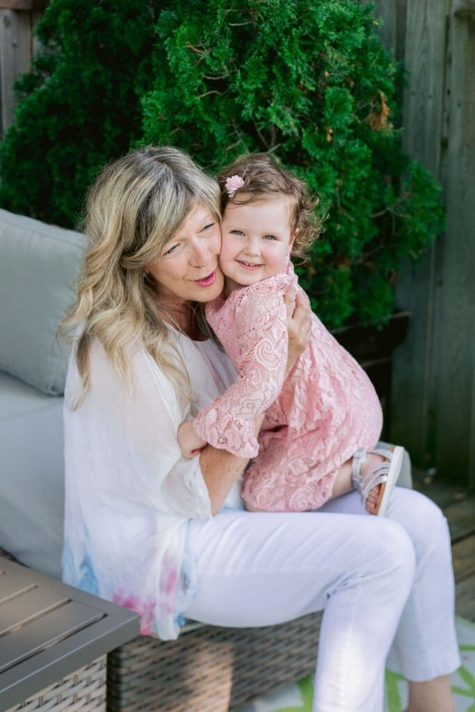 A grandmother holding her smiling granddaughter on her lap while sitting on patio furniture.