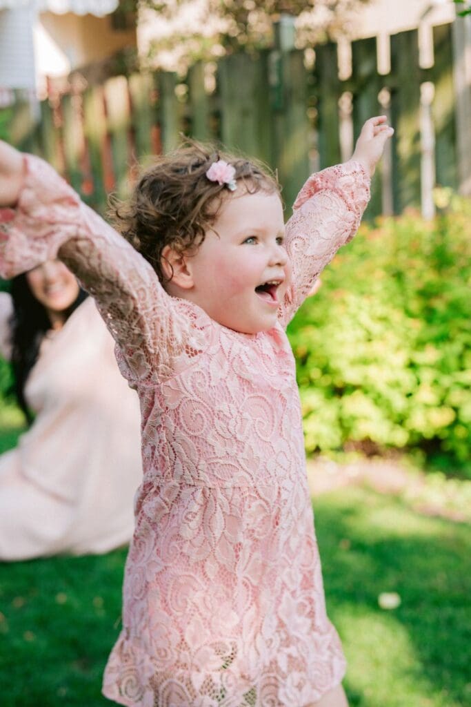 Young girl in pink lace dress with arms raised joyfully