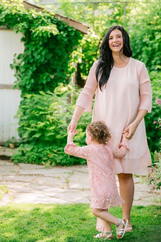 Young girl in pink lace dress reaching out to her pregnant mother in a blush dress outdoors.