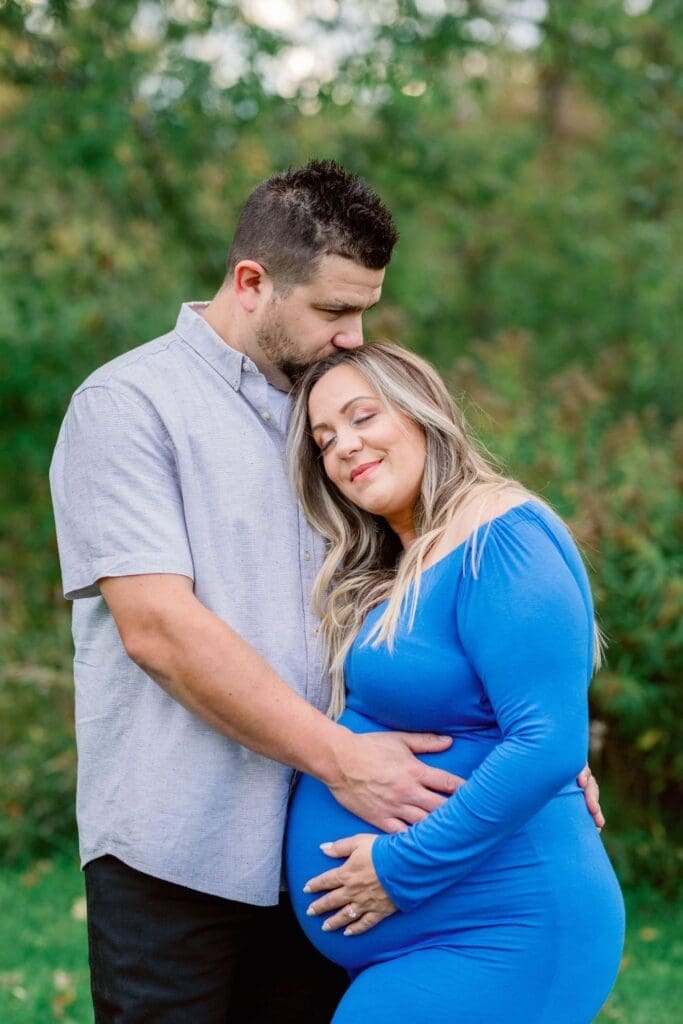 Close-up of hands on pregnant belly in a royal blue maternity dress.