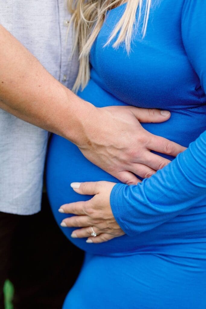 Couple embracing during a maternity session with woman in blue gown and man kissing her head.