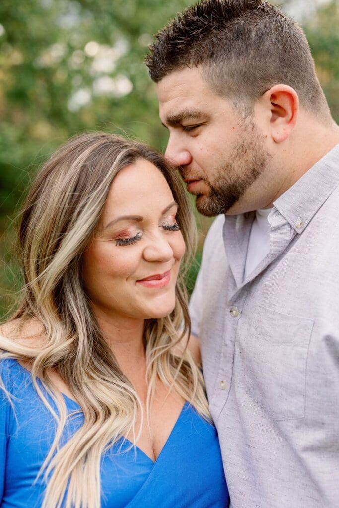 A close-up of a pregnant woman smiling softly with her eyes closed while her partner leans in lovingly, outdoors.