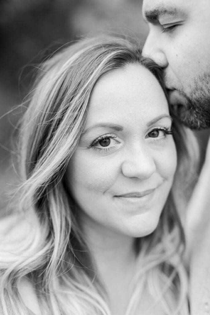 Black and white close-up of smiling pregnant woman being kissed on the forehead.