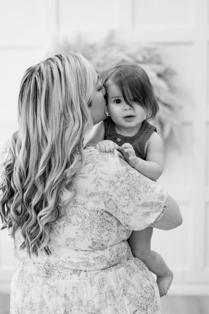 Black and white photo of a mother holding her son and kissing his cheek as he looks directly at the camera.