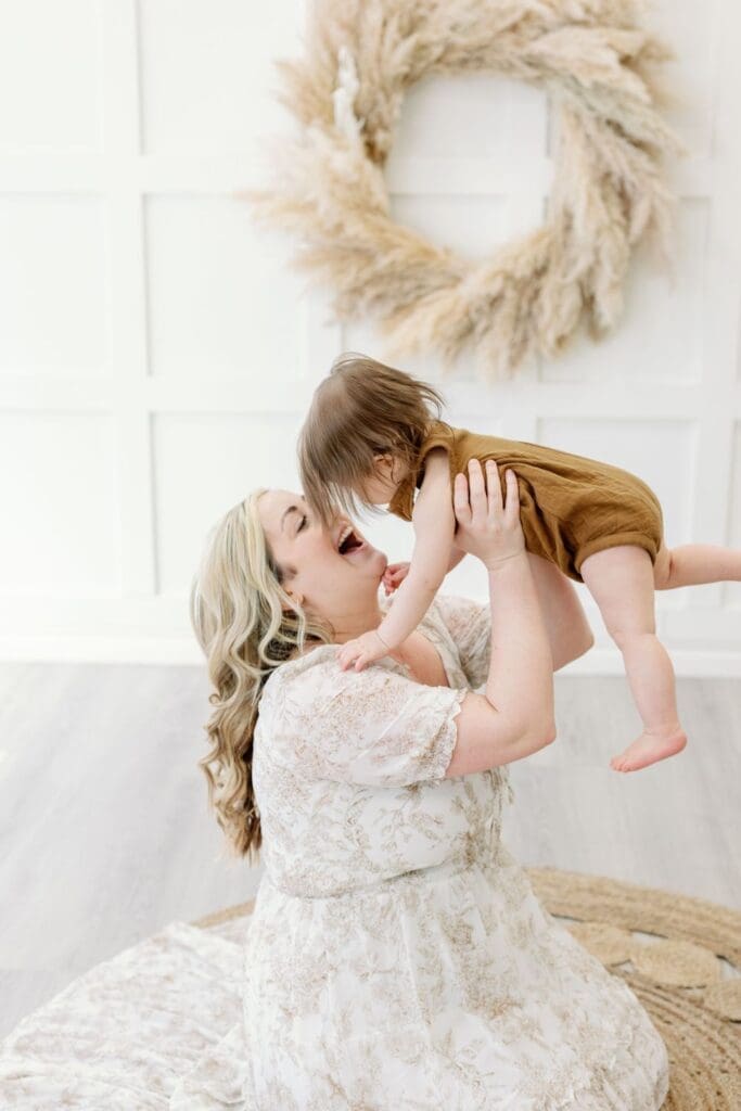 A joyful mother lifts her baby  into the air, both laughing and playing during a family studio session.