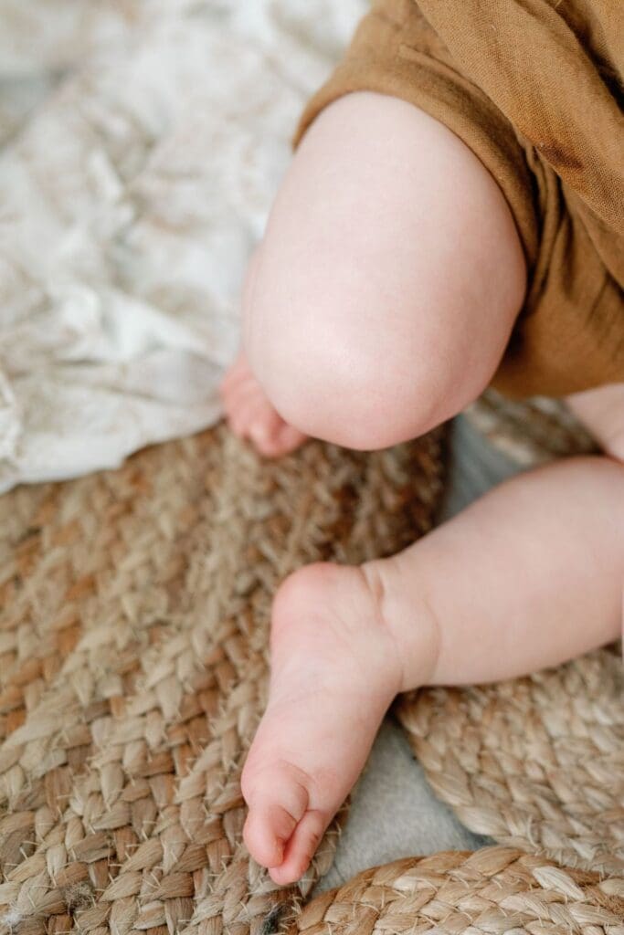 Close-up of baby’s chubby legs and feet on a woven jute rug during a studio session.