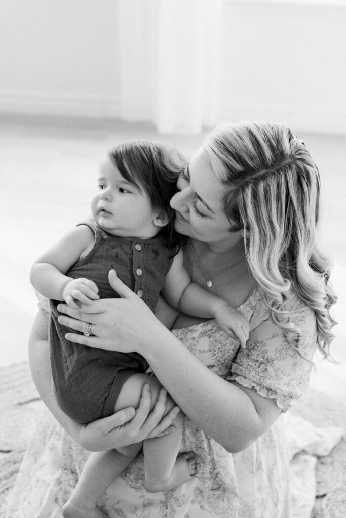 A mother sits on the floor, gently holding her toddler in a heartfelt moment of connection and comfort, captured in black and white.