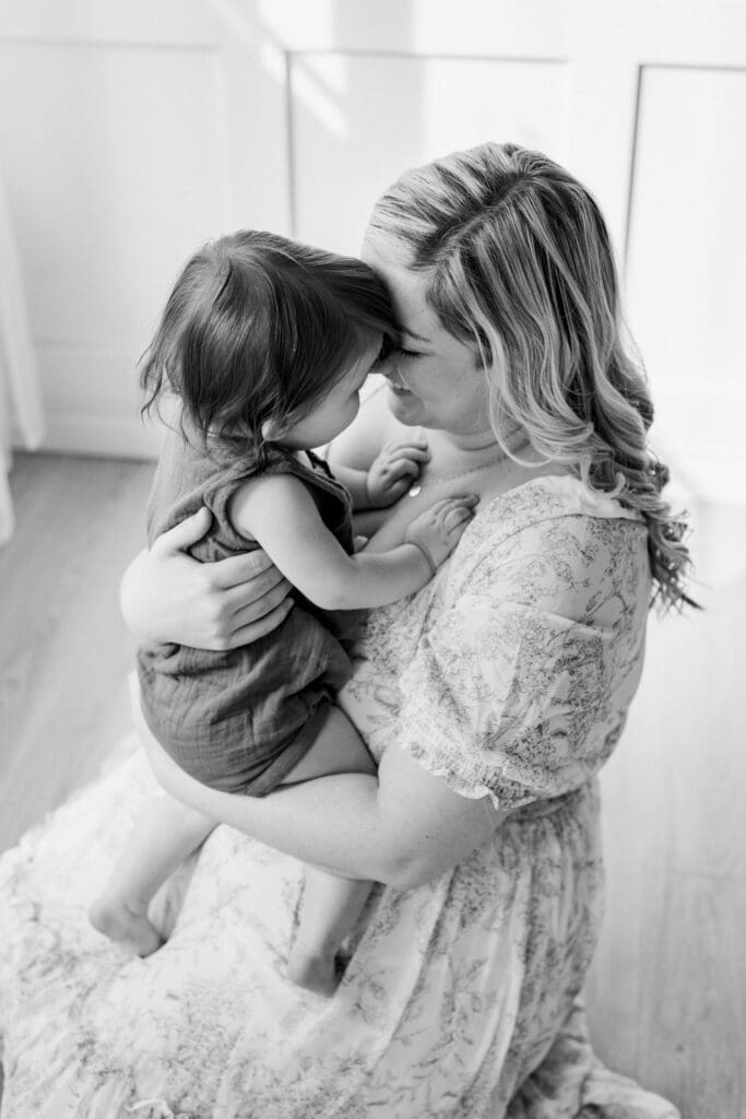 Close-up of mother and toddler touching foreheads, smiling during a motherhood studio shoot.