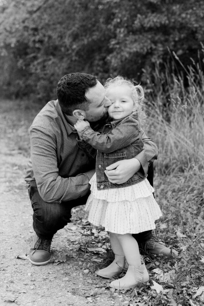Dad leaning in to kiss daughter, her arms around his neck.