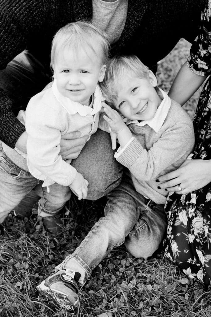 Older brother smiling while embracing his younger sibling during a family photo session on grass.